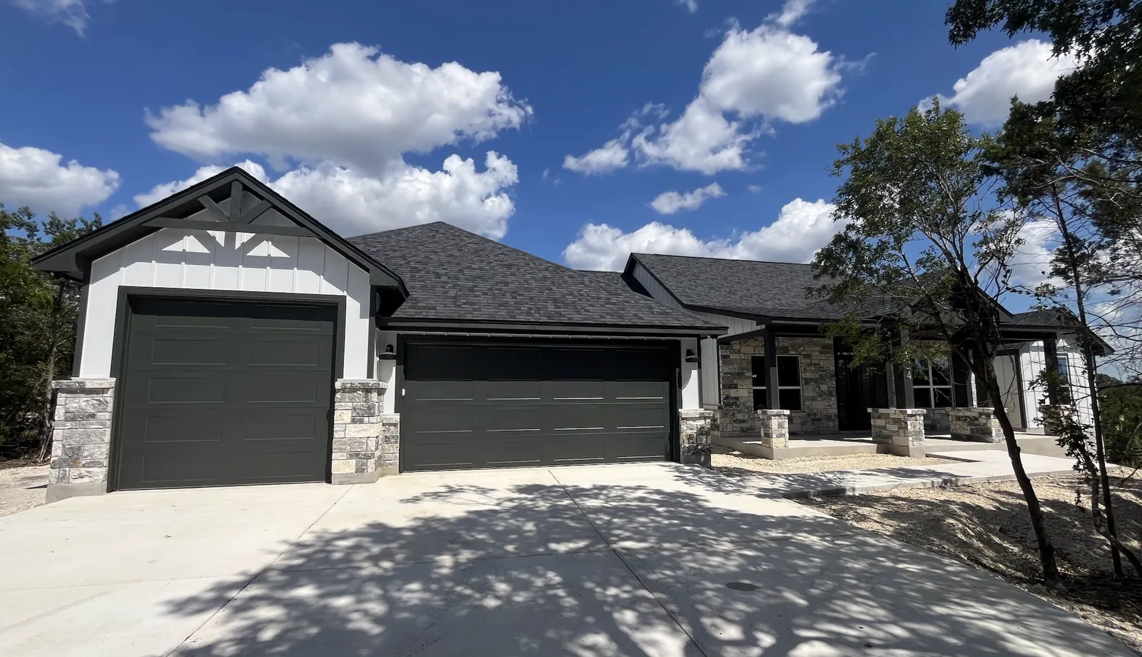 Front of the Vaughn custom home in Fischer: board-and-batten gables, stone columns, a covered front porch and a three-car garage