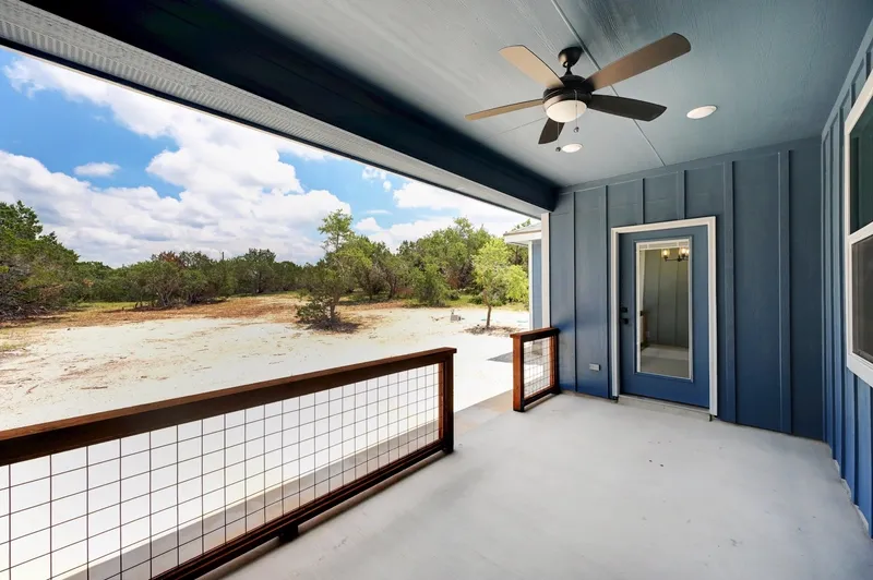 Covered porch with a ceiling fan and cable railing looking out over cleared Hill Country