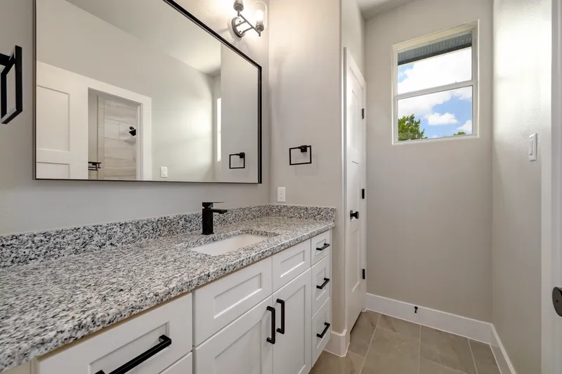 Guest bathroom with a granite vanity and framed mirror under a window