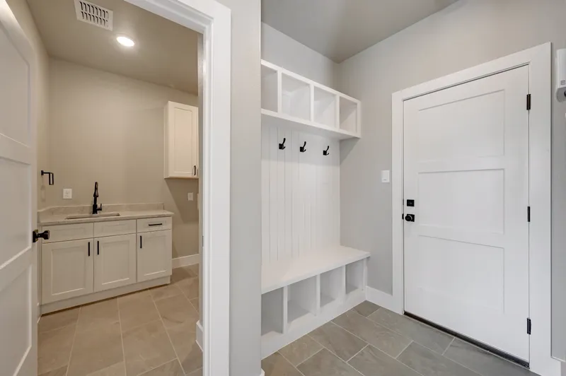 Mudroom drop zone with a built-in bench, coat hooks, open cubbies and a sink cabinet